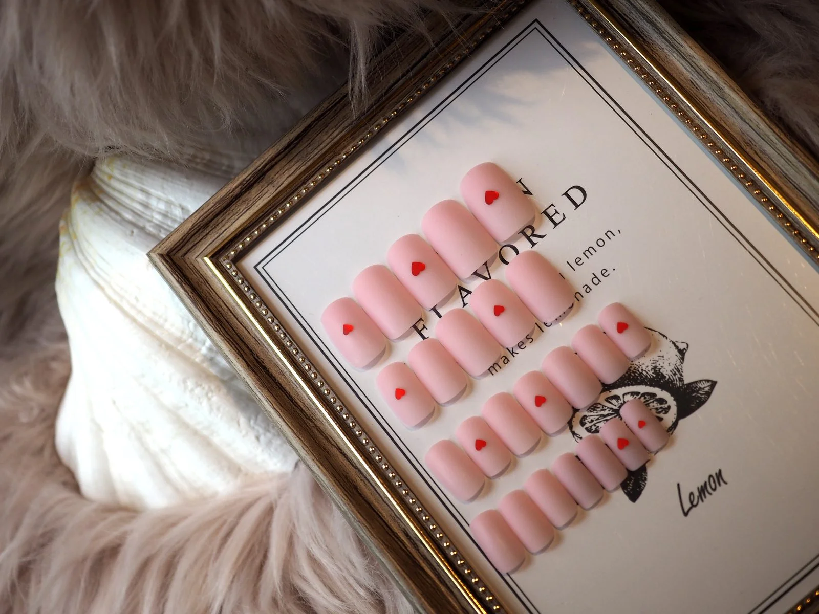 Matte pale-pink press-on nail set with tiny red hearts, displayed in a gilt frame